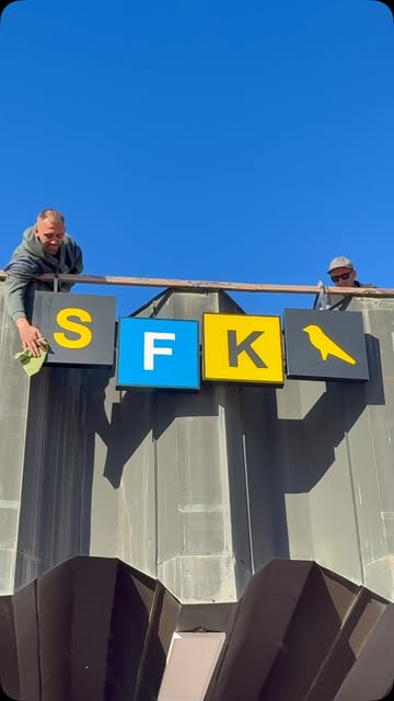 The SFK sign being fixed to a building against a blue sky